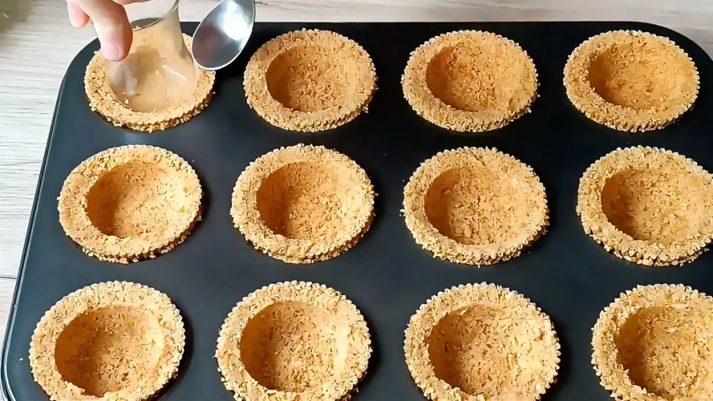 Pressing the nut and biscuit mixture into paper molds for No-Bake Chocolate Strawberry Cups