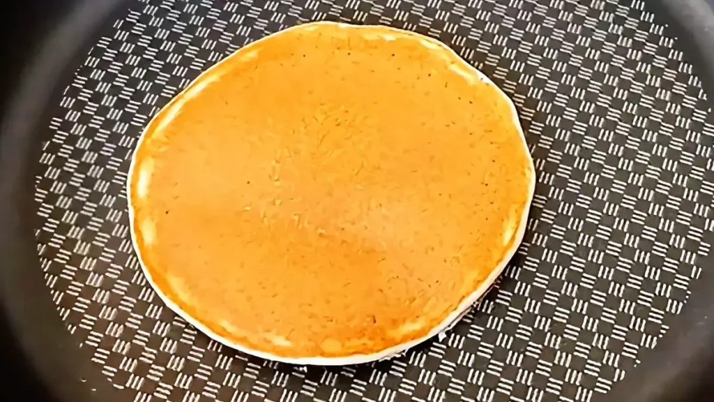 Golden pancakes cooking in a non-stick pan on the stove prepared for breakfast